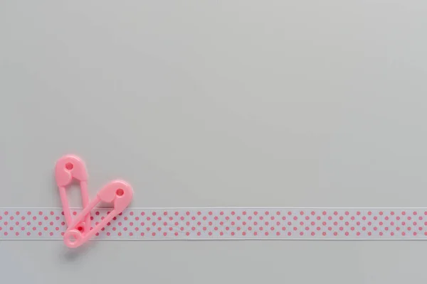 baby girl concept border with pink and white polka dot ribbon and pink toy plastic disper safety pins on white background