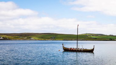 Lerwick, Shetland - 12 Temmuz 2024: Lerwick açıklarında suda oturan Dim-Riv adlı bir Viking teknesindeki Bressay Adası 'na bakıyorum..