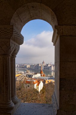 Macaristan 'ın Tuna Nehri ve Budapeşte kentindeki Balıkçı Kalesi' ndeki kemerlerin birinden Macar Parlamento Binası manzarasına bakıyorum.