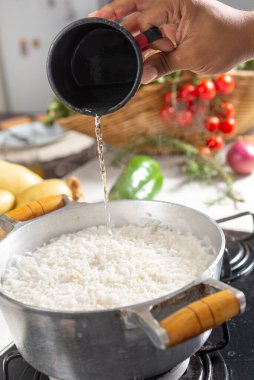 Arka planda malzemeler olan tavaya beyaz pirinç döken bir kadın.