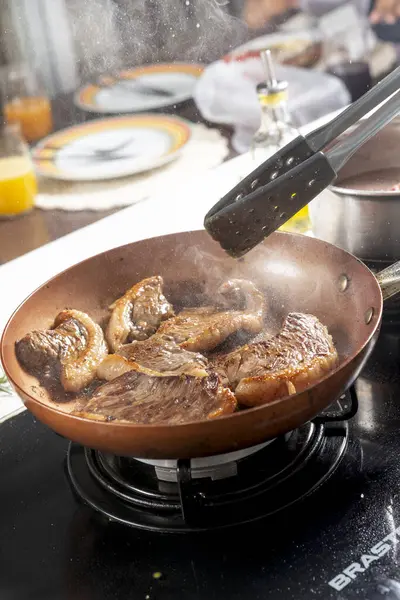 Şef, restoranın mutfağında tavada biftek pişiriyor.