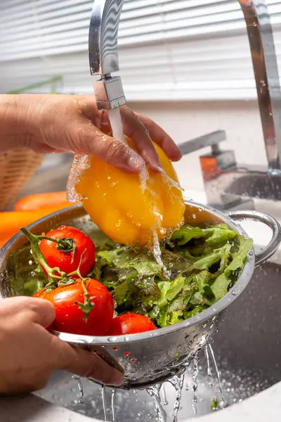 Ev mutfağında biber, marul ve domates yıkayan eller.