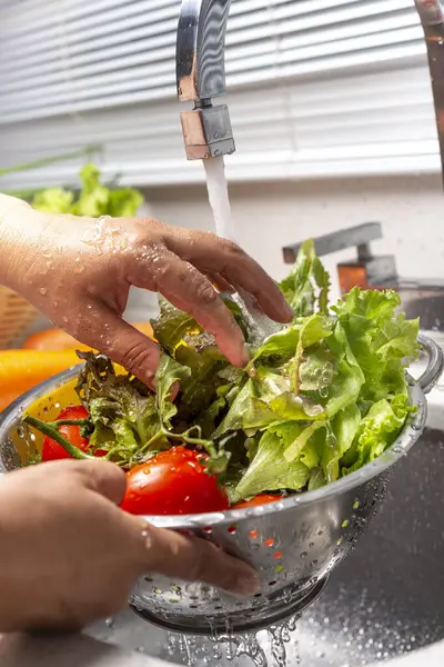 Ev mutfağında biber, marul ve domates yıkayan eller.