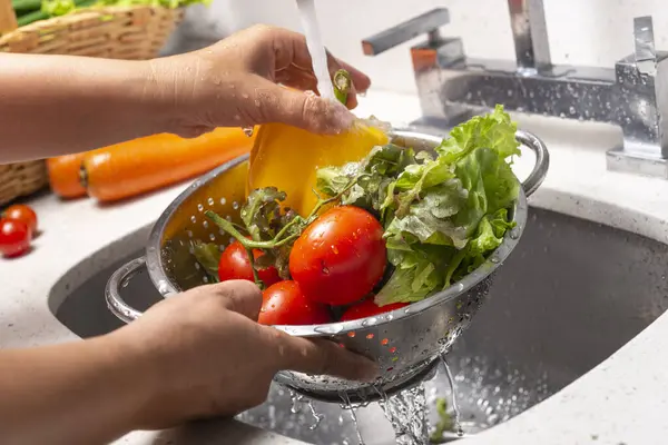 Ev mutfağında biber, marul ve domates yıkayan eller.