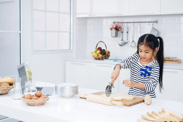Smiling Asian little asian girl child is learning and enjoying for baking cookies bakery on wooden Cutting board in kitchen. Homemade pastry for bread. Family love and Homeschool.