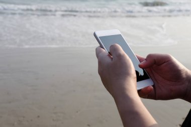 Kapalı el kamerasında akıllı telefon ve internetteki internet ve deniz kenarındaki iş gezileri için ekrana dokunuyor. Tatil konsepti teknolojisiyle tatil ve rahatlama