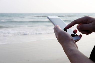 Kapalı el kamerasında akıllı telefon ve internetteki internet ve deniz kenarındaki iş gezileri için ekrana dokunuyor. Tatil konsepti teknolojisiyle tatil ve rahatlama