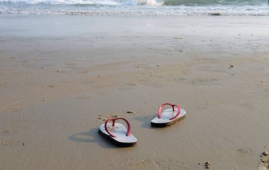 Sandaletler ve ayakkabı izleri plajda ve mavi denizde.