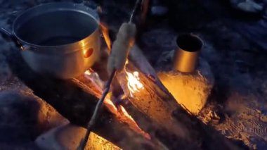 Gece kamp ateşi yakan bir adam kamp ateşi yakar ve karanlık ormanda ızgara pilavla yemek pişirir.