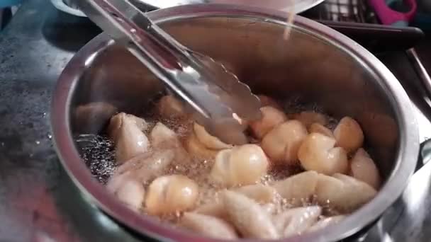 アジアの商人の手で閉じ込められた深い揚げられた肉球はタイの市場の街路の食糧で顧客に美味しい食糧を販売するために沸騰油の鍋でです — ストック動画