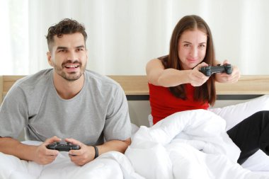 Gülümseyen Kafkasyalı genç aşıklar, ellerinde joysticklerle oyun oynuyorlar. Yatak odasında birlikte eğleniyorlar. Tatilde evlilik hayatı ilişkisi kavramı