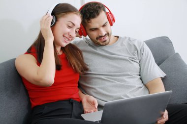 Gülümseyen Kafkas aşığı çift oturma odasında kulaklık ve dizüstü bilgisayarla online müzik dinliyor. Tatilde evlilik hayatı ilişkisi kavramı