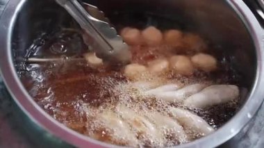 Asyalı tüccarların ellerinde, Tayland pazarında müşterilere lezzetli yiyecekler satmak için kaynar yağda kızartılmış köfteler var.