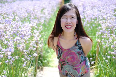 Güzel Asyalı kadın gülümsüyor ve gevşiyor Mor Murdannia Giganteum çiçek tarlasında