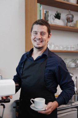 Gülümseyen Kafkas genç barista adam önlük giyiyor ve kahve ve kahve sipariş eden müşteriler için makineyle kahve yapıyor. Küçük bir kafe ve teknoloji işletmesi kurun