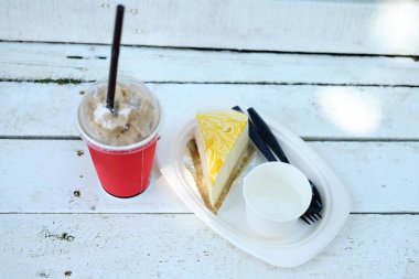 Taze buzlu kahve, kırmızı bardakta, peynirli kek ve kremalı kafe ve kafede ahşap bankta.