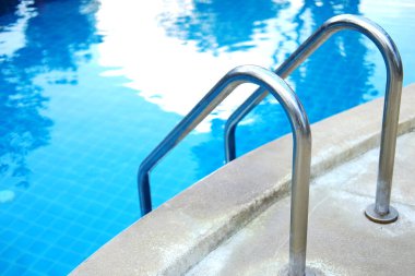 Mavi suda paslanmaz çelik korkuluklar ve açık havuzda seramik fayanslar tatil köyü ve otel bahçesinde.