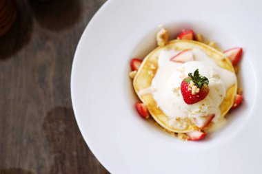 Kafe ve pastanede beyaz tabakta vanilyalı dondurmalı ev yapımı çilekli krep. Üst görünüm