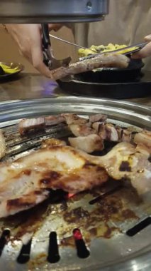 Kadın elinin yakınında Kore usulü ızgara restoranda ızgara domuz eti kesmek için makas kullanıyor.