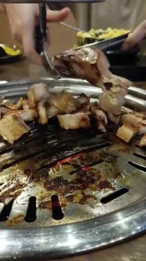 Kadın elinin yakınında Kore usulü ızgara restoranda ızgara domuz eti kesmek için makas kullanıyor.