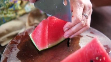 Asyalı kadın elini, tahta kesme tahtasındaki taze karpuz dilimleri ve parçaları kesmek için bıçak kullanarak kapat.