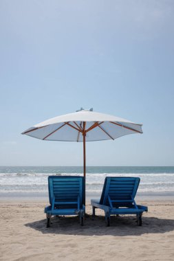 Yazın Asya 'da güneşli bir günde kumsalda, beyaz şemsiyelerin altında birkaç şezlong ve tropikal sakin deniz.