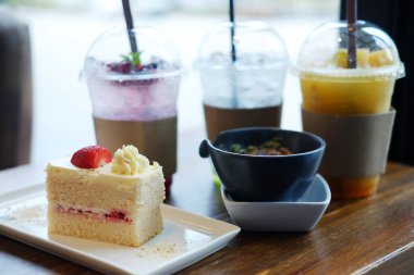 Bir parça vanilyalı kek taze pişmiş çilekli kremalı fırınlanmış ıspanak peynirli ve limonatalı buzlu soda kafede plastik bardakta.