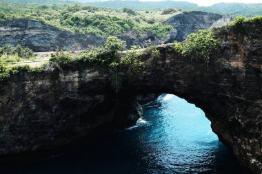 Endonezya, Bali, Endonezya ve Nusa Penida plajlarında gezmek için dağda ve mavi denizde delikleri olan kayalık bir mağaranın güzel manzarası.