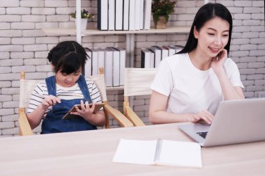 Bilgisayarla çalışan gülümseyen Asyalı anne ve kızı evdeki ofis odasında tabletle oyun oynuyorlar. Evde eğitim kavramı için çocuk eğitimi