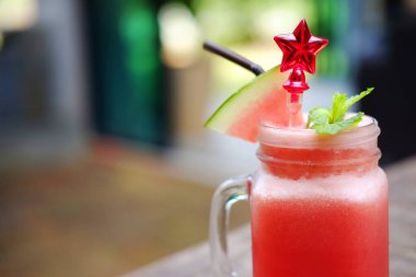 Kafedeki ahşap masada kırmızı yıldız kaşıklı bir bardak karpuz smoothie 'sini kapat. Boşluğu kopyala