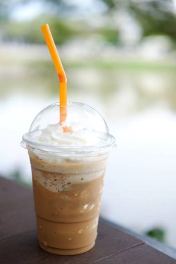 Krem şantili buzlu sütlü kahve. Plastik bardakta tüp. Tahta masa üzerinde.