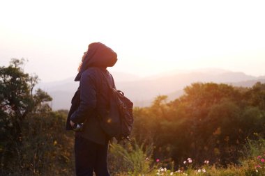 Elinde kamera olan Asyalı genç bir kadın. Yanında kır çiçeği ve Tayland 'ın Chiang Mai Eyaleti' nin Doi Luang Chiang Dao Dağı 'nın güzel manzarası var. 