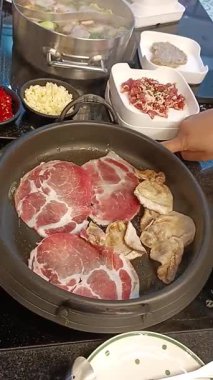 Kadın eli, Kore restoranındaki sıcak tavada domuz eti pişiriyor. Clip 'in Dikey