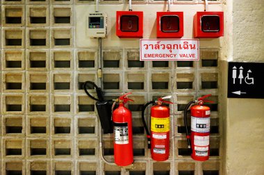 Taylandlı karakterlerde kırmızı yangın söndürücü ve beton duvarda tuvalet etiketi olan acil durum valfleri.