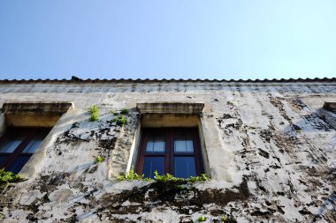 Vintage ve kırsal grunge beton duvarlı eski işlenmiş demir pencere. Eski evlerin ve mavi gökyüzünün dışı.
