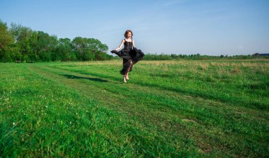 A young red-haired woman in a black dress cheerfully runs across the field.