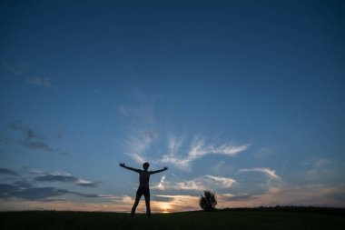 Silhouette of a young man against the background of the evening sky and the setting sun.