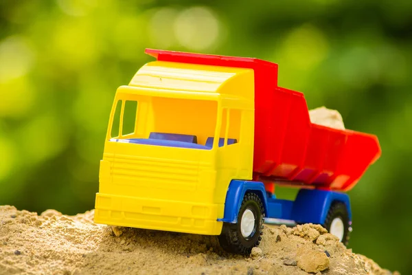 Children\'s toy truck in the sand on a blurred green natural background.