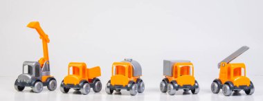 Construction vehicles lined up in a row. Multi-colored children's toys plastic trucks on a white background.