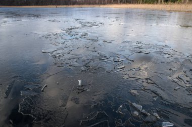 The texture of thin melting ice on a spring lake with the sky reflected on the surface. Light glare.