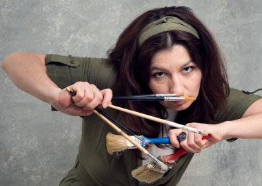 Ressam, yeşil tulumlu ve stüdyo arka planında fırçayla boyanmış bir kadın..