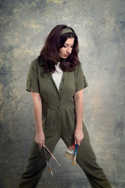 Ressam, yeşil tulumlu ve stüdyo arka planında fırçayla boyanmış bir kadın..