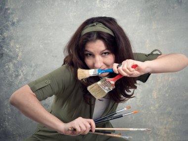 Ressam, yeşil tulumlu ve stüdyo arka planında fırçayla boyanmış bir kadın..