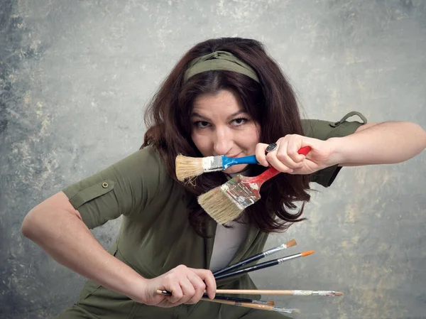 Ressam, yeşil tulumlu ve stüdyo arka planında fırçayla boyanmış bir kadın..