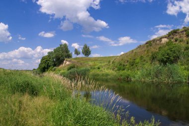 Dik kıyıları olan bir nehir yatağı ve kümülüs bulutlu mavi bir yaz gökyüzü..