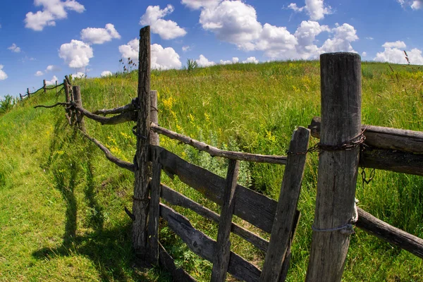 Wooden fence on the green hills against the blue sky.