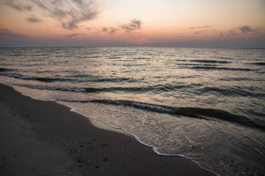Şafakta kıyıda. Alacakaranlık. Köpüklü karanlık dalgalar.