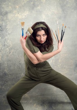 Ressam, yeşil tulumlu ve stüdyo arka planında fırçayla boyanmış bir kadın..