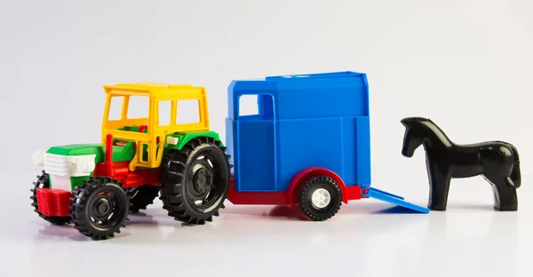 Plastic toy multi-colored tractor with a van for transporting horses on a white background.