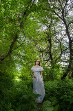 Ormanda güneşin altında, şeffaf beyaz elbiseli bir kız. Yumuşak odak.